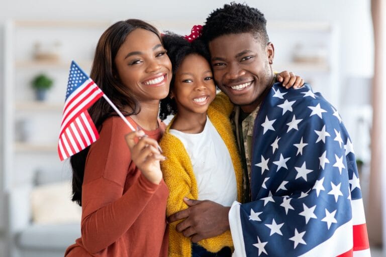 black military man wrapped in flag posing with wife and little daughter